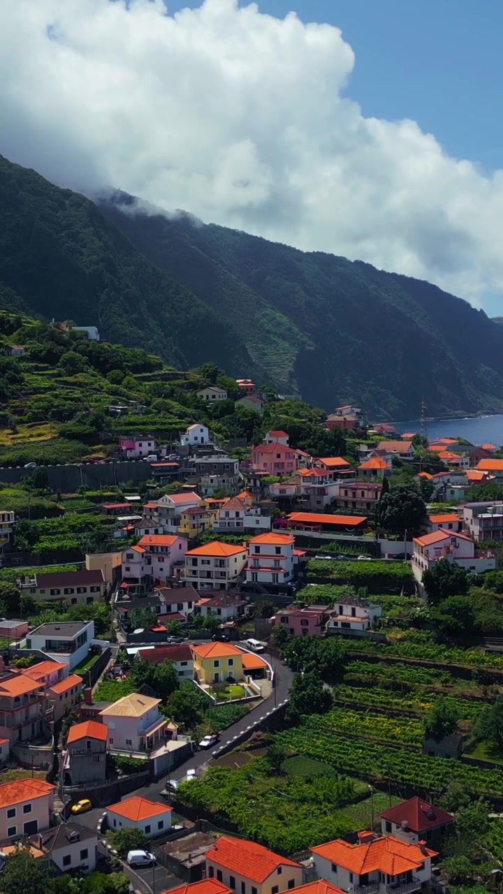 Freguesia de São Vicente no Seixal, Madeira, Portugal, mostrando casas na encosta, vegetação em socalcos e formações de nuvens dramáticas acima da paisagem montanhosa, vista aérea vertical.