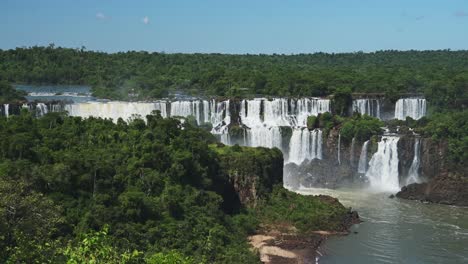 dramatische entfernte aussicht auf wunderschöne wasserfälle in malerischen dschungelgrünen landschaft, weite szene von wasserfällen, die von riesigen klippen in wunderschönen sonnigen bedingungen in iguazu falls, brasilien, fallen