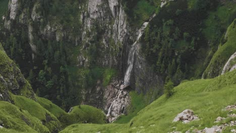 Toma-Estática-En-Cámara-Lenta-De-Una-Cascada-Que-Cae-En-Un-Valle-De-Montaña-Con-Un-Paisaje-Alpino