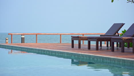 Peaceful-view-of-a-poolside-with-a-wooden-deck-and-lounge-chairs-next-to-the-sea