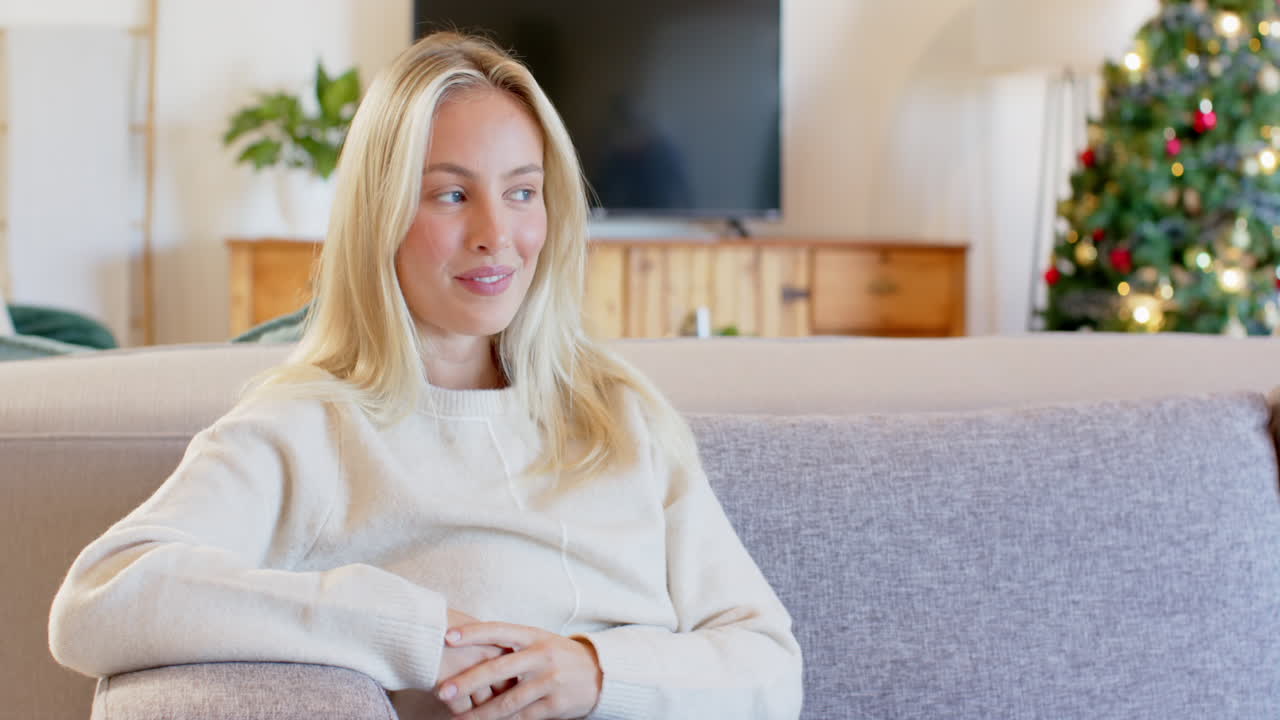Woman relaxing on sofa at home, Christmas tree glowing in background