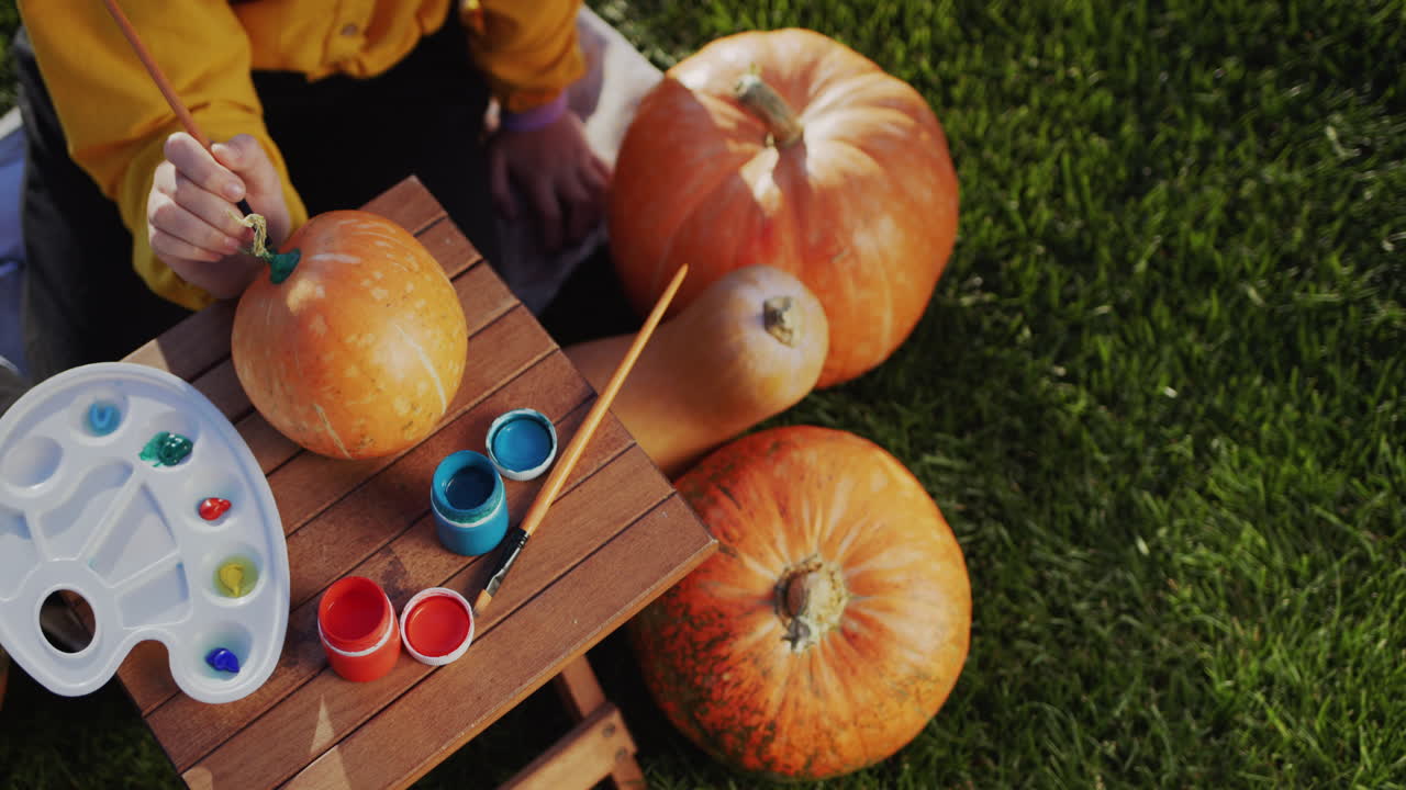 Child's hands with a paintbrush paint pumpkins. Preparing decorations for Halloween