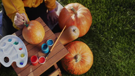 child's hands with a paintbrush paint pumpkins. preparing decorations for halloween