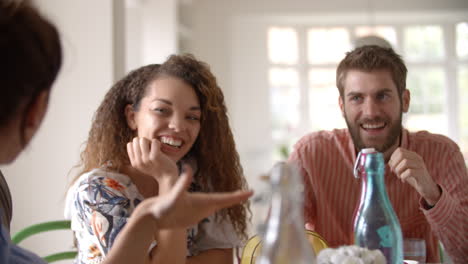 Panning-shot-of-young-adult-friends-talking-at-dining-table