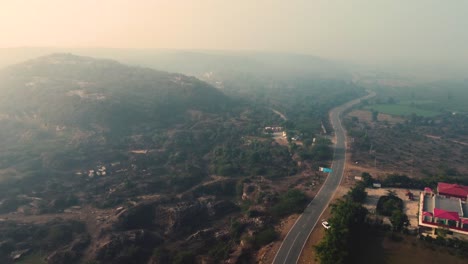 tomada aérea de un avión no tripulado de una carretera de un pueblo a través de colinas boscosas durante el amanecer en la india central