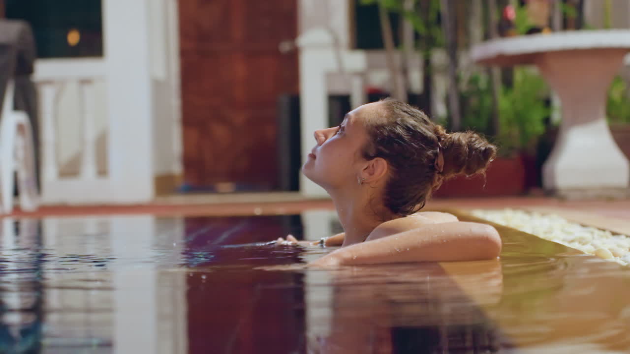Donna in piscina in un resort sull'isola, riflessione serale e quieta contemplazione vicino a lettini e piante tropicali, leggere increspature dell'acqua, viaggiatrice solitaria rilassata che si gode l'atmosfera calma del resort.