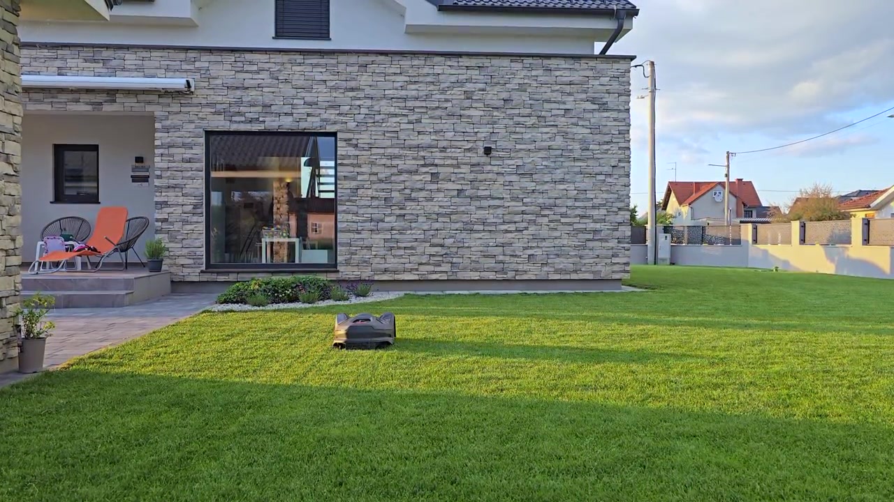 Robot tagliaerba automatico che taglia l'erba verde brillante in un moderno giardino residenziale. Tecnologia per la casa intelligente e attrezzature da giardinaggio autonome