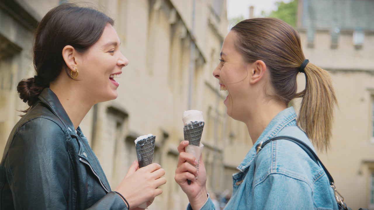 Coppia di donne che visita i luoghi e mangia gelati mentre passeggiano insieme per Oxford, Regno Unito.