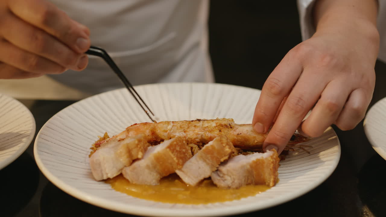 A professional chef carefully places a prawn on a plate of black rice accompanied by pieces of juicy pork