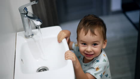 smiling kid opened the tap in the bathroom. joyful toddler learning to use the faucet. top view.