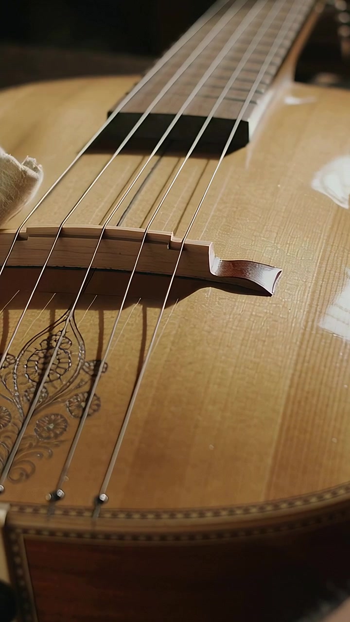 Vertical video: Spotting smudges, player hands wiping guitar top and bridge in dim room with cloth