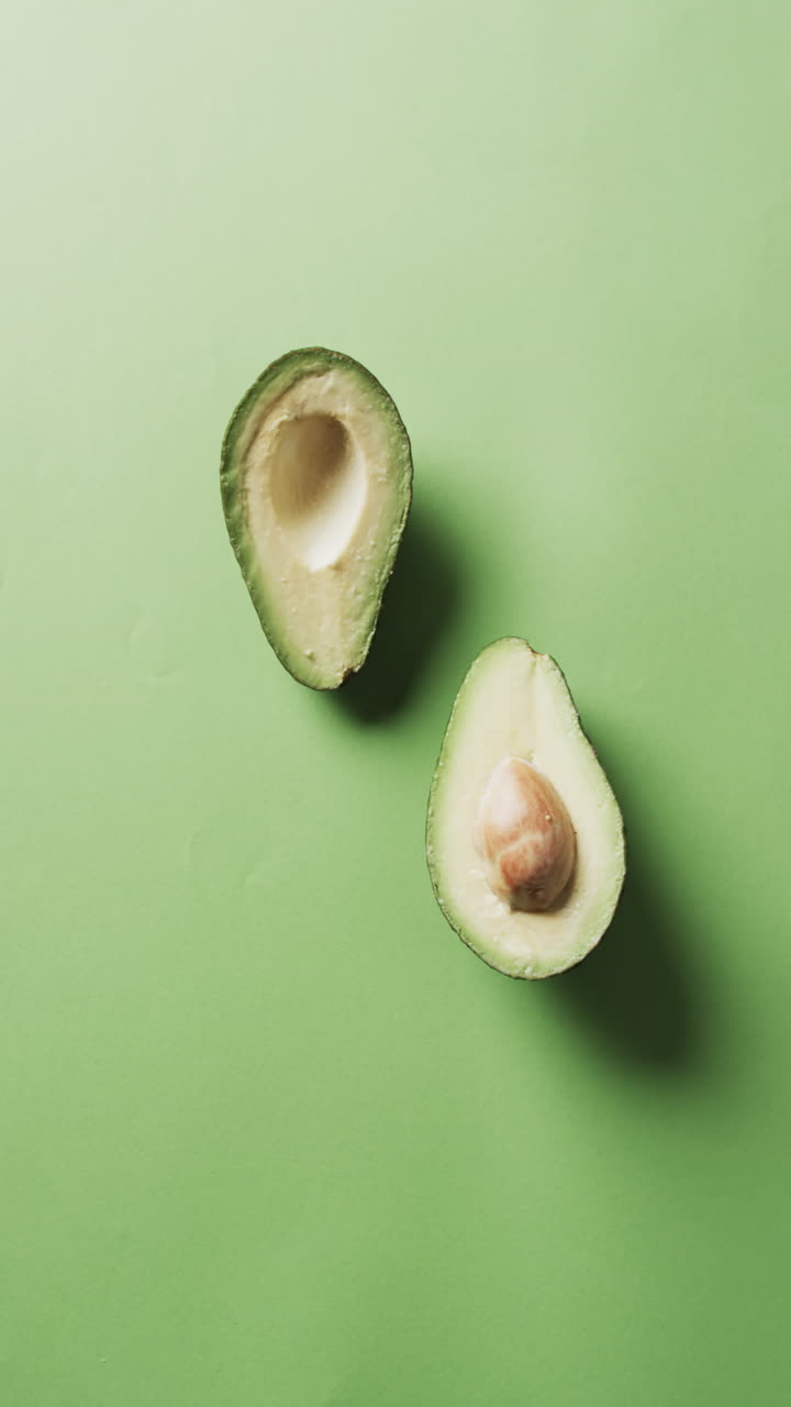 Vertical video of sliced avocado with copy space over green background