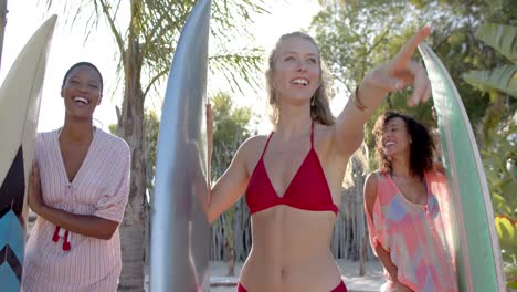 Portrait-of-happy-diverse-group-of-friends-holding-surfboards-on-sunny-beach