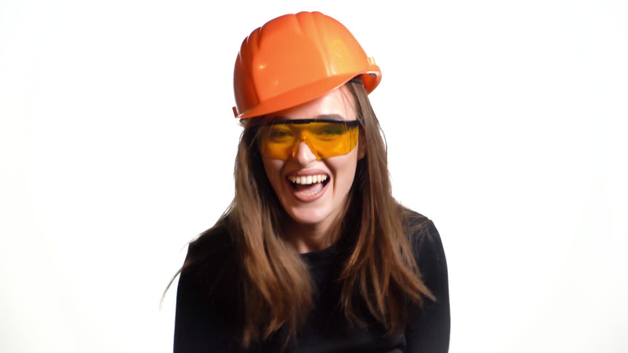 Cheerful girl engineer in black jumper and a bright helmet emotionally talks about business, with gesturing and holding a folder-holder and a pen in her hands on a white background.