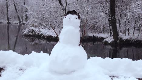 a snowman on the river bank in the middle of the european forest with gentle snowfall - trucking shot