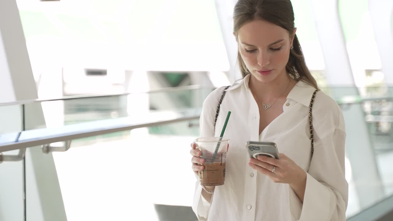mujer joven bebiendo café y usando el teléfono en un edificio moderno
