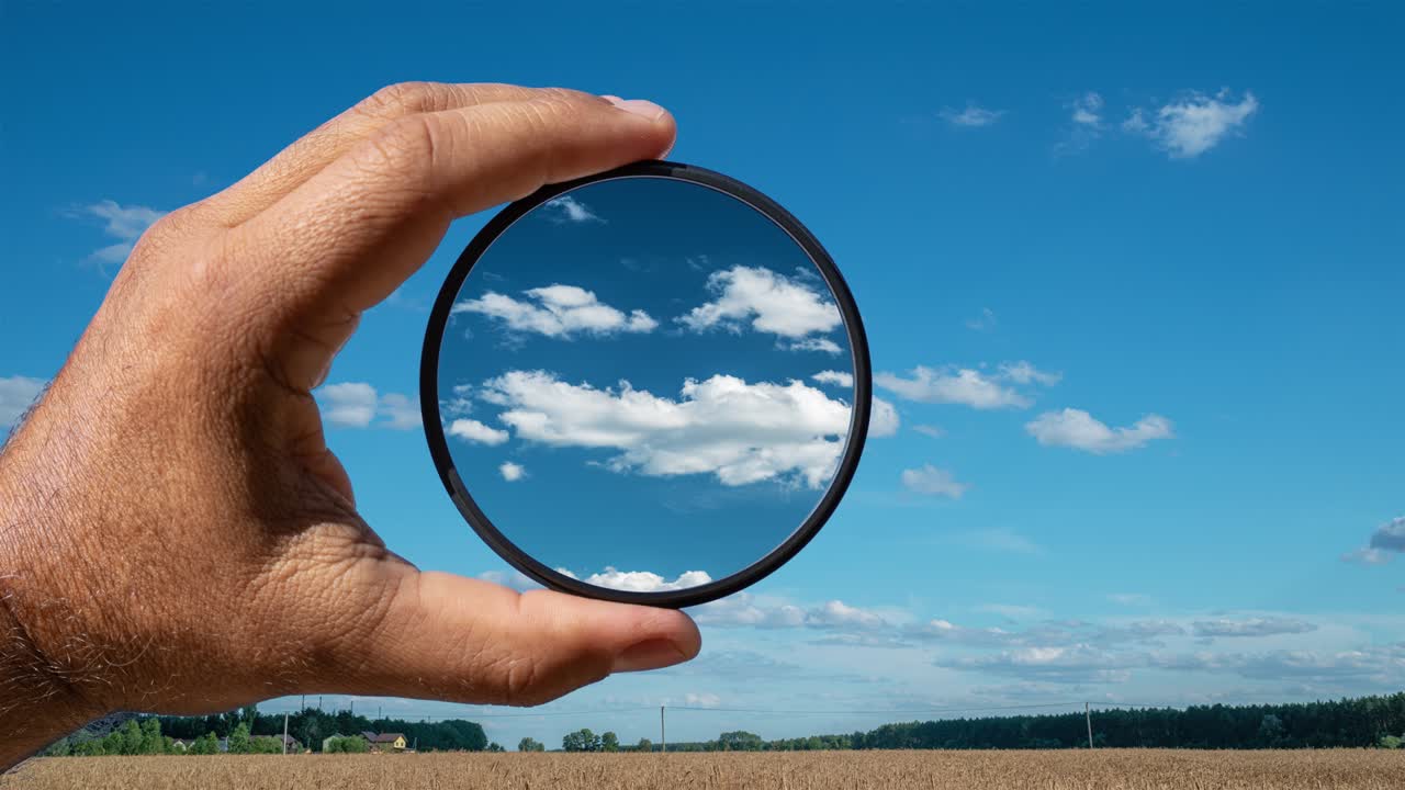 efecto visual del filtro polarizador en el ejemplo de un paisaje rural de verano con hermosas nubes. la mano sostiene un filtro circular, aplicando el efecto de polarización.