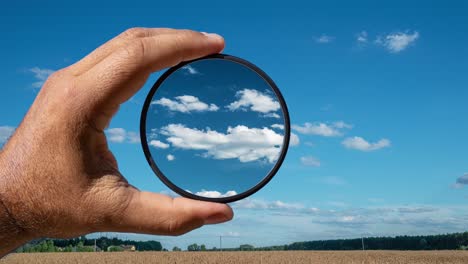 visual effect of the polarizing filter on the example of a summer rural landscape with beautiful clouds. the hand holds a circular filter, applying the polarization effect.