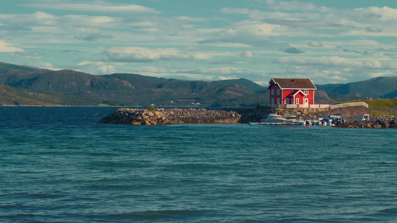 Scenic red wooden house in a fjord, Norway. Cinemagraph of blue ocean with harbor pier and boats and ships.