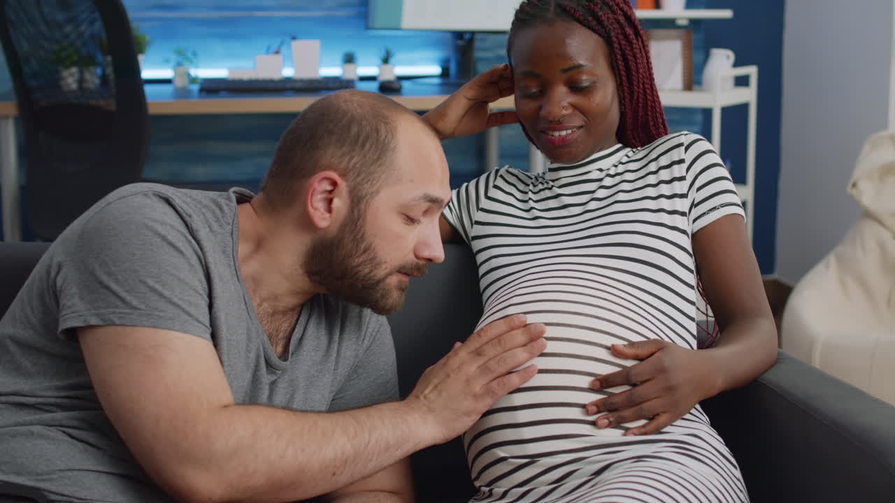 Young interracial parents sitting together on couch