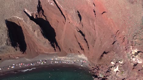 vista aérea de la playa roja llena de turistas y bañistas, santorini