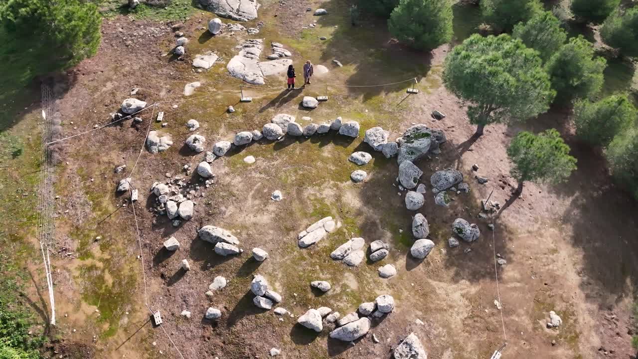 vuelo con un dron en un cromlech de piedras de granito con una forma circular que está envasada con una cuerda y hay dos personas que lo visitan