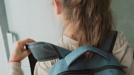 mother helps daughter secure backpack straps by fridge while brother finishes pulling book‑laden backpack onto shoulder ready for school morning in cozy home environment filled with natural light and soft decor