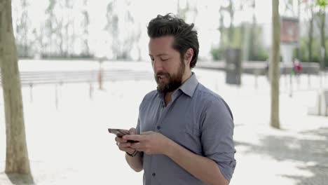 Smiling-bearded-man-using-mobile-phone-outdoor