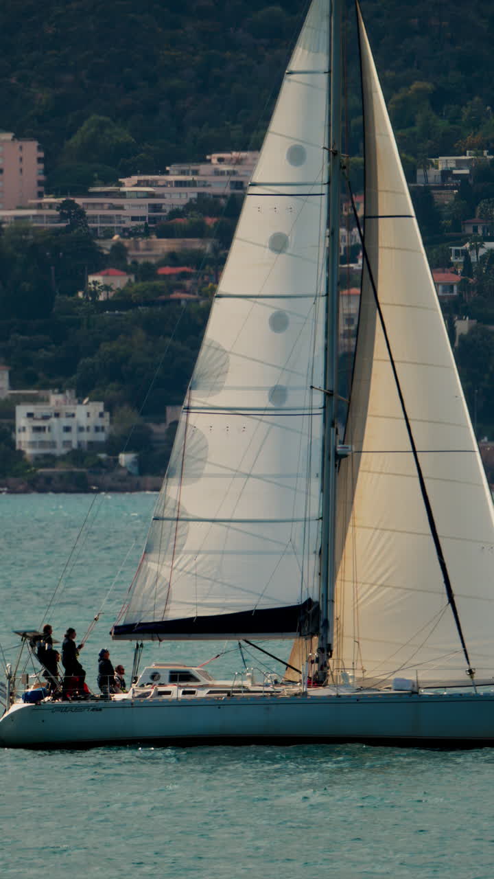 Juan-les-Pins, Francia - 3 aprile 2025: barca a vela che si muove sul mare con la città e la montagna sullo sfondo. Verticale