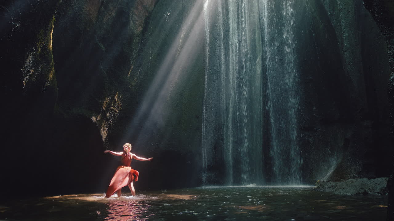 donna che balla in una grotta di cascate spruzzando acqua indossando un bel vestito godendo della natura ballando sentendo la libertà spirituale 4k