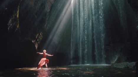 dancing woman in waterfall cave splashing water wearing beautiful dress enjoying nature dance feeling spiritual freedom 4k