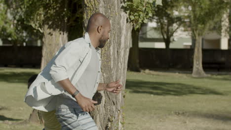 Happy-black-father-and-son-running-around-tree,-playing-outdoors