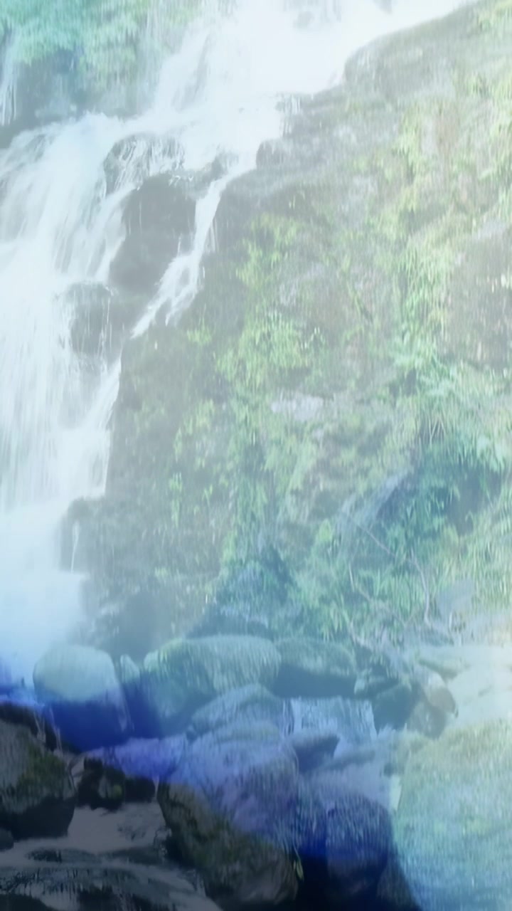 縦型動画：カメラが下へパンし、滝が岩棚を分かれて流れ落ち、川底が見える。