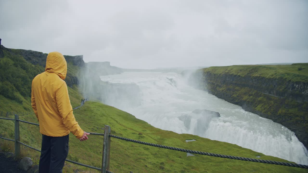 turista masculino con impermeable amarillo disfrutando de la cascada de gullfoss en islandia. concepto de fondo de viaje