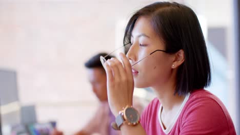 thoughtful asian female creative working at computer in casual office, slow motion