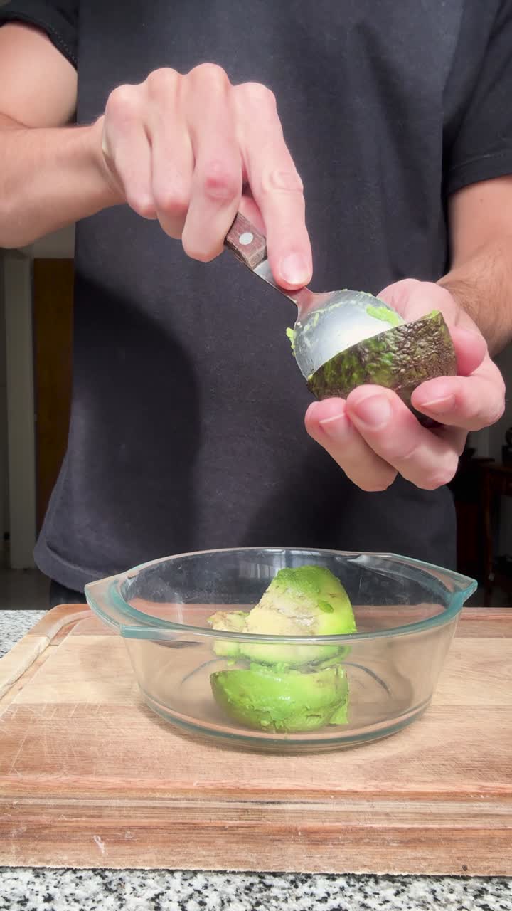 Vertical close up shot of a man removing the pulp from an avocado with a spoon