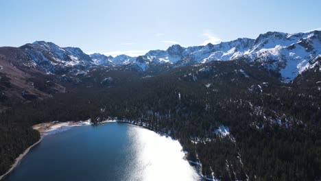 drone flying towards snowy mountains over alpine lakes in mammoth lakes california