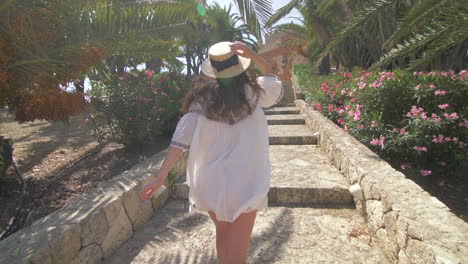 woman in a straw hat walking up stairs in a beautiful garden