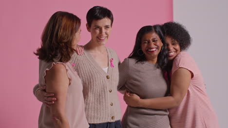 studio portrait of multi-racial group of women of different ages wearing pink breast cancer awareness ribbons hugging against pink background 2