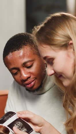 lovely young family of white woman and african-american man looks at baby ultrasonic pictures in living room close view slow motion