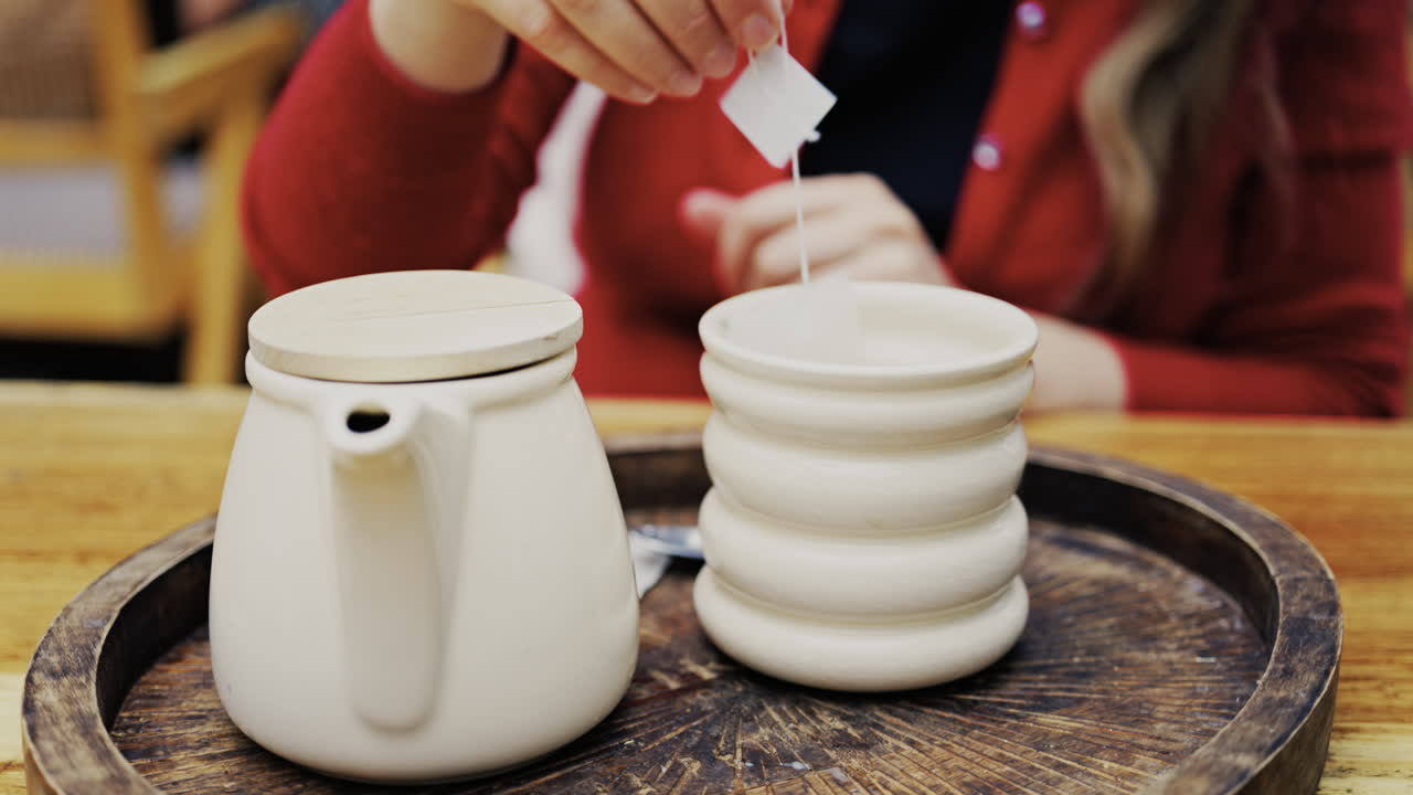 Close up of a woman in a red suit putting a tea bag in a white cup on a wooden tray