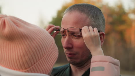 a heartwarming scene where a little girl in a pink beanie and jacket adjusts her father's glasses, showing a tender moment of care and connection between them. the man, wearing a green jacket