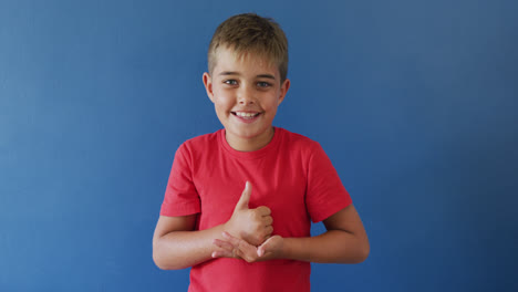 niño caucásico feliz usando lenguaje de señas en fondo azul, cámara lenta