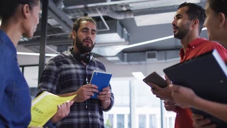 Diverse-group-of-work-colleagues-standing-holding-documents-and-tablet-talking