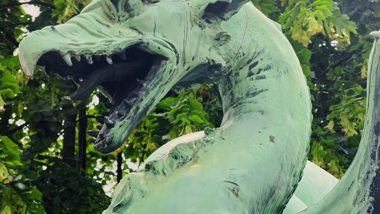Primo piano della testa di drago in bronzo sul Ponte dei Draghi di Lubiana, che mostra il simbolo mitico della città contro alberi verdi in Slovenia
