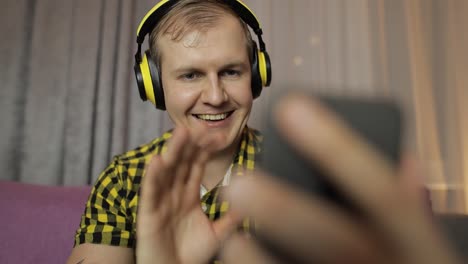 young man making selfie, talking, video call at home in wireless headphones