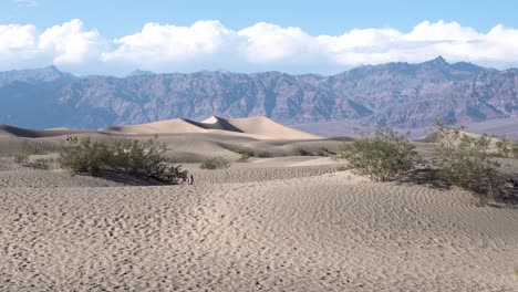 sand dunes of the mojave desert with people exploring the area, aerial rising shot