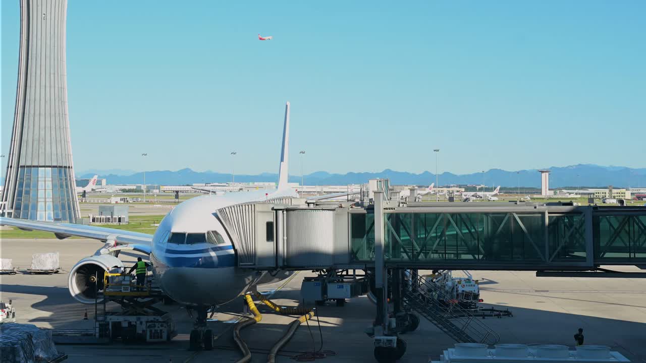 In the daytime, a commercial plane is parked on the runway at Beijing International Airport, China, with clear skies above and airport facilities, including the control tower, visible in the distance.