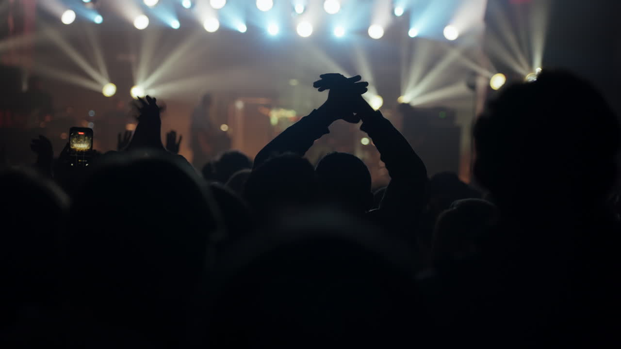 Público en silueta aplaudiendo en un concierto de música en vivo.