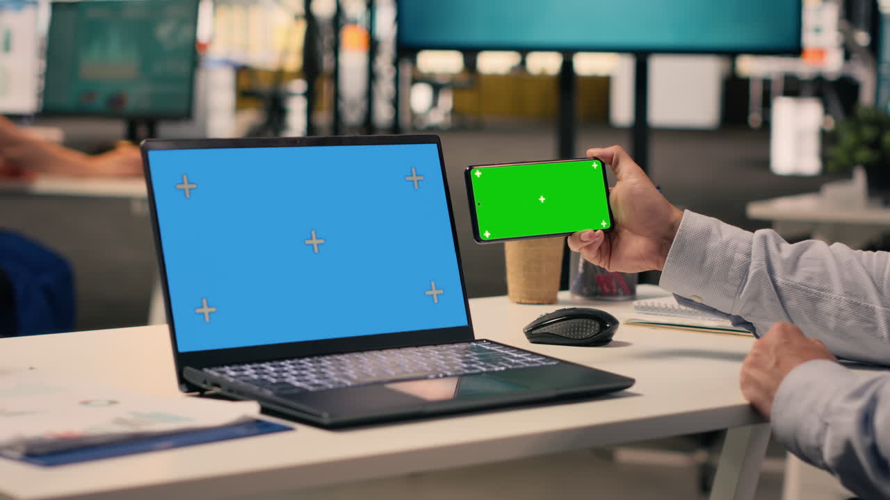 Chroma key su telefono e schermo blu su laptop alla scrivania con uomo d'affari